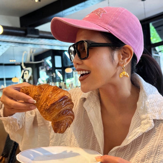 Woman in a pink cap and sunglasses holding a croissant in a casual setting